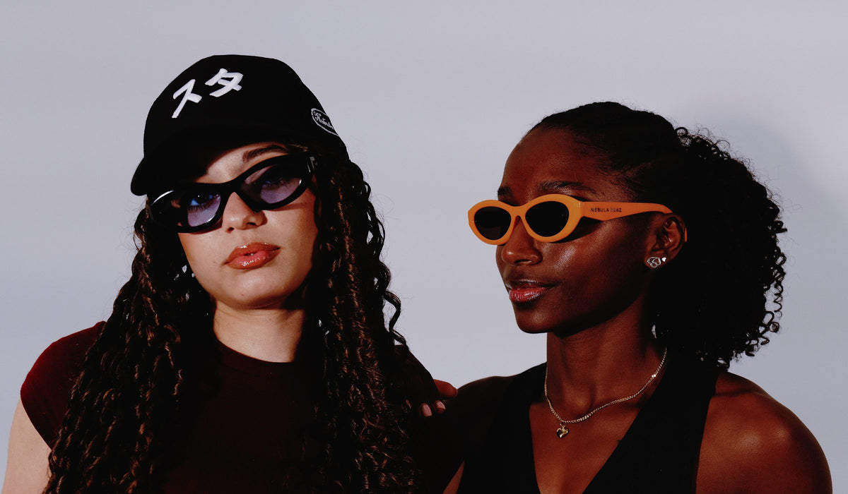 Dos modelos con gafas de sol y gorra Sutā de Nebula Reaz sobre fondo neutro